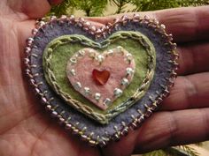 a hand holding a felt heart ornament with beads and sequins on it