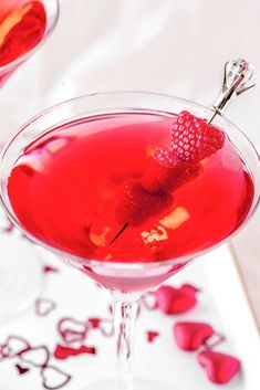 two martinis with raspberries in them on a white tray and red hearts