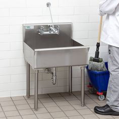 a person with a mop is cleaning the floor in front of a stainless steel sink