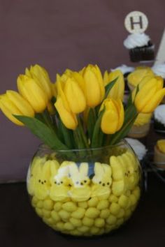 a vase filled with yellow flowers sitting on top of a table next to cupcakes