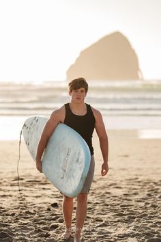 a young man holding a surfboard on the beach in front of an ocean cliff