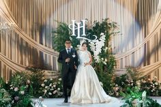 a man and woman standing in front of a floral arch with the word h on it