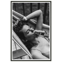 a black and white photo of a woman laying in a chair drinking from a bottle