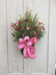 a pink and red bow hanging on the side of a white door with flowers in it