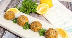 three meatballs with parsley and lemon on a white platter next to sliced lemons