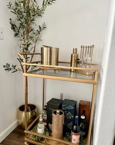 a gold bar cart filled with bottles and liquors next to a potted plant