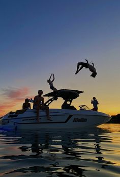 two people jumping off the back of a boat into the water at sunset with their arms in the air