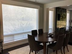 a dining room table and chairs in front of a large window with blinds on it