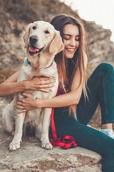 a woman sitting on top of a rock holding a dog