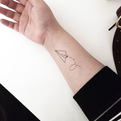 a person's arm with a paper airplane tattoo on the left side of their wrist