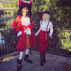 two women dressed in costume standing next to each other near a fence and water area