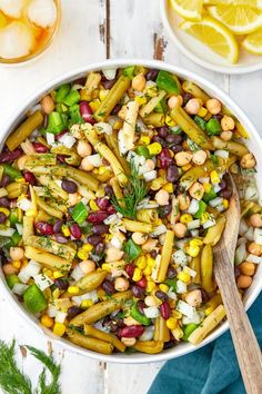 a white bowl filled with beans and vegetables next to lemon wedges on a wooden table