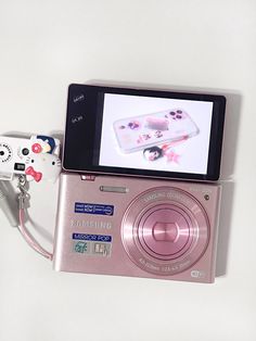 a pink camera sitting on top of a white table next to a video game controller