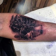 a man's arm with a tattoo of an elk and pine trees on it