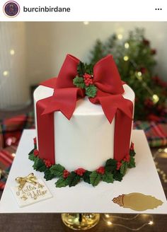 a white cake with red ribbon and holly decorations on top, sitting on a table