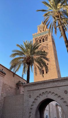 a tall tower with a clock on it's side next to palm trees and a building