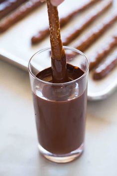 a person dipping some kind of hot dog into a glass filled with dark chocolate sauce