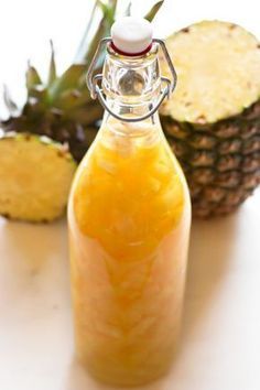 a pineapple juice in a glass bottle next to some cut up pineapples