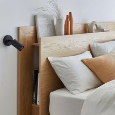 a bed with white sheets and pillows next to a wooden headboard on the wall