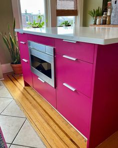 a kitchen with pink cabinets and white counter tops, an oven and potted plants