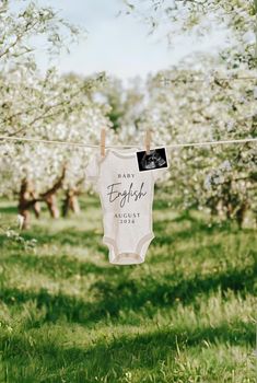 a babysuit hanging on a clothes line in an orchard with blossoming trees behind it