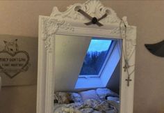 a white mirror sitting on top of a wall next to a bed under a window