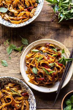 two bowls filled with noodles and vegetables next to chopsticks on a wooden table