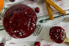 cranberry sauce in a glass jar next to cinnamon sticks and orange juice on a white wooden table