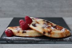 two pancakes topped with raspberries on top of a black slate slabd counter