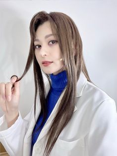 a woman with long brown hair wearing a white lab coat and blue turtle neck sweater