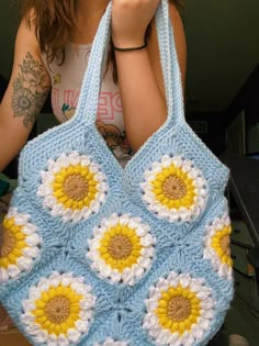 a woman is holding a crocheted bag with sunflowers on the front