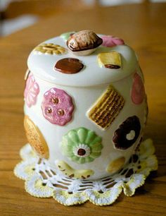 a decorative ceramic container sitting on top of a wooden table next to a doily