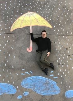 a woman holding an umbrella over her head while standing on the sidewalk with chalk drawings