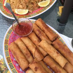 two plates filled with food next to a bowl of rice and some dipping sauce on the side