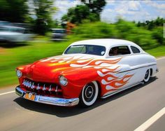 a red and white car with flames on it's hood driving down the road