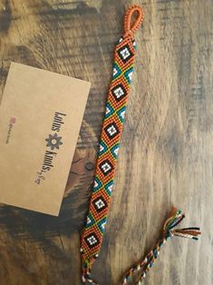 an orange, blue and white beaded bracelet on a wooden table next to a card