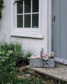 two cement boxes with flowers in front of a door and window on the side of a house