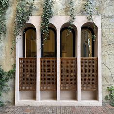 three windows with wooden screens and ivy growing on the side of a building, in front of a brick wall