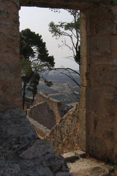 an open window in the side of a stone building with trees and hills in the background