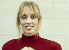 a woman in a red top smiling at the camera with her hands on her hips