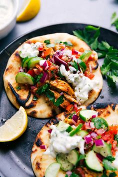 two pita breads topped with chicken, vegetables and sour cream sauce on a black plate