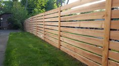 a wooden fence in the grass next to a sidewalk