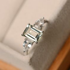 This ring features a 6*8mm emerald cut green amethyst and sterling silver finished with rhodium. Customization is available. It is made by hand, and it will take about 7 days to finish the ring after your payment is completed. Main stone: green amethyst Main stone weight: Approx 1.60 ct Metal type: sterling silver finished with rhodium Accent stone: CZ Customization is available, I also can make it with 14k solid gold (white or yellow or rose), just feel free to contact me. Any question, just le Luxury Green Multi-stone Amethyst Ring, Green Amethyst Engagement Ring, Amethyst Ring Engagement, Green Emerald Ring, Green Amethyst Ring, Round Engagement Rings, Three Stone Ring, Gem Ring, Quartz Ring