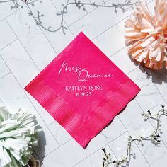 a pink napkin with the names of two people on it sitting next to some flowers