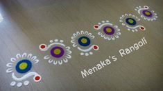 the name merka's rangoli written in white and blue on a brown floor