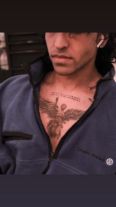 a man with a bird tattoo on his chest wearing a blue sweatshirt and earrings