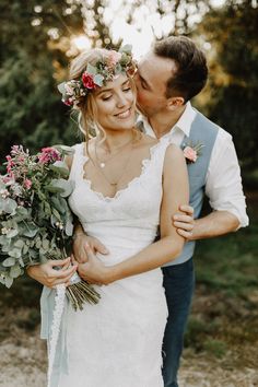 a bride and groom embracing each other in front of some trees with flowers on their heads