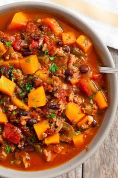 a white bowl filled with chili and sweet potato soup on top of a wooden table