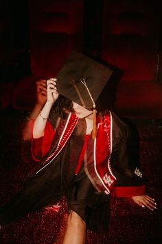 a woman in a graduation cap and gown is sitting on the floor with her hands behind her head