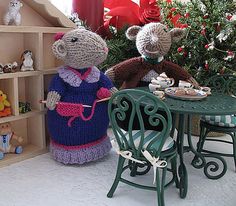 two knitted mice sitting at a table in front of a doll house